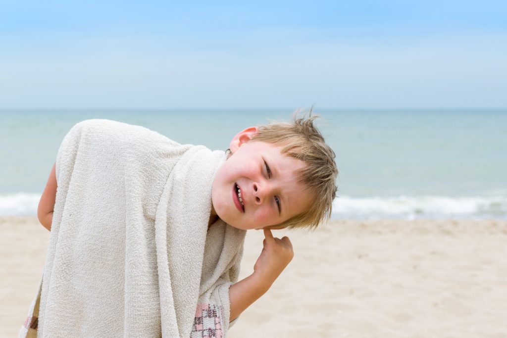 A little boy cleans his ear from the water by the sea, ocean.